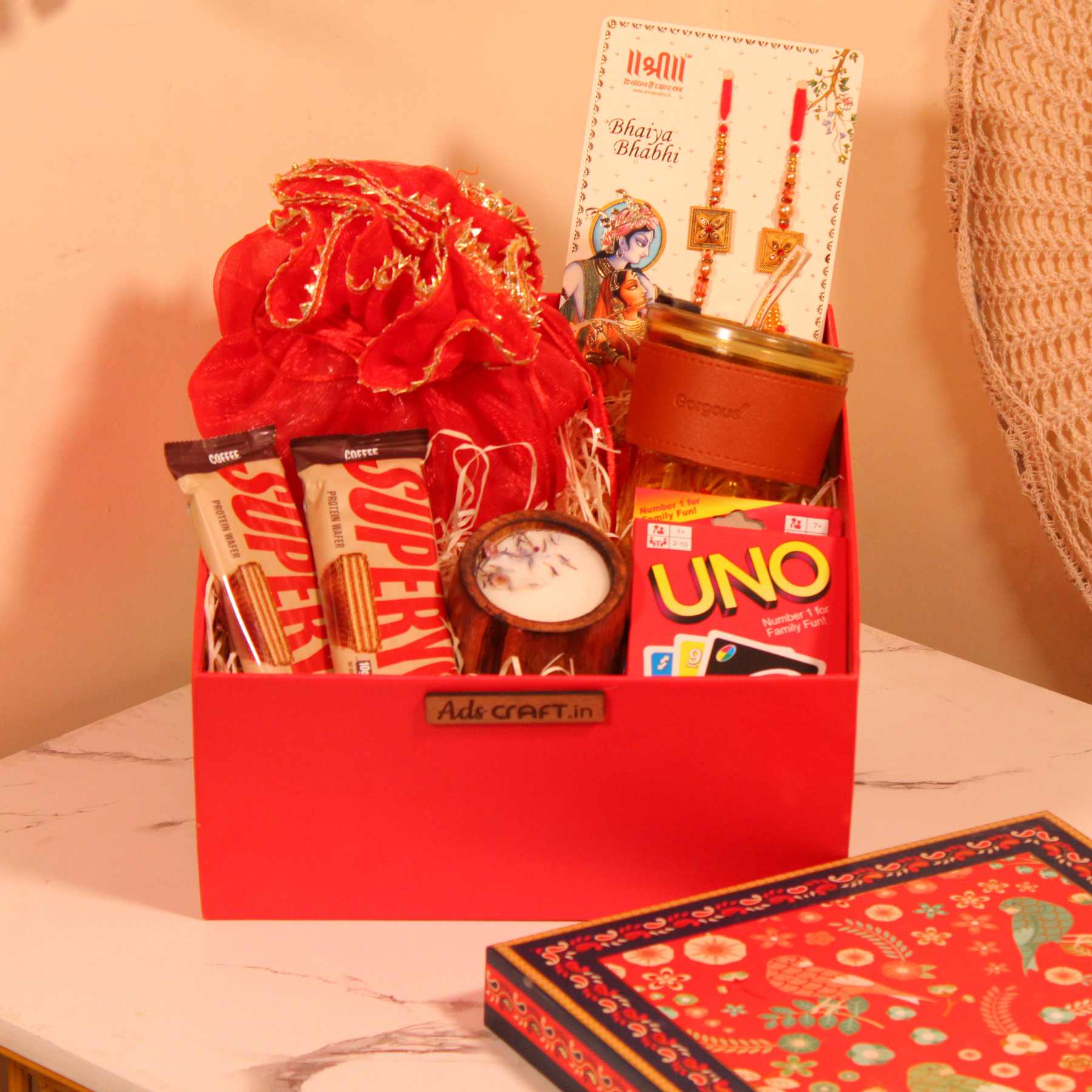 Rakhi gift hamper for Bhaiya Bhabhi in a red box with couple rakhi, dry fruits, UNO cards, and cookies.