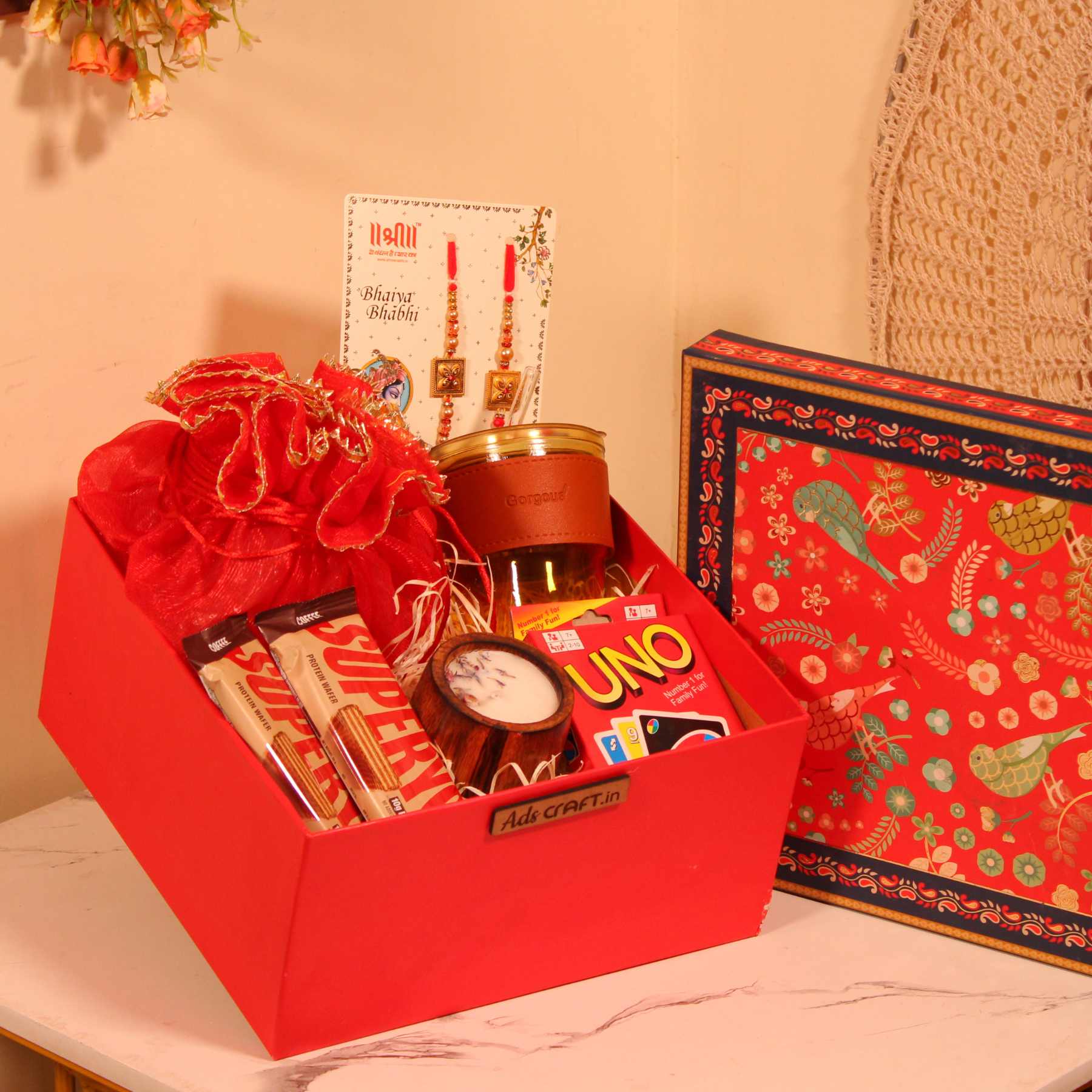 Rakhi gift hamper for Bhaiya Bhabhi in a red box with couple rakhi, dry fruits, UNO cards, and cookies.