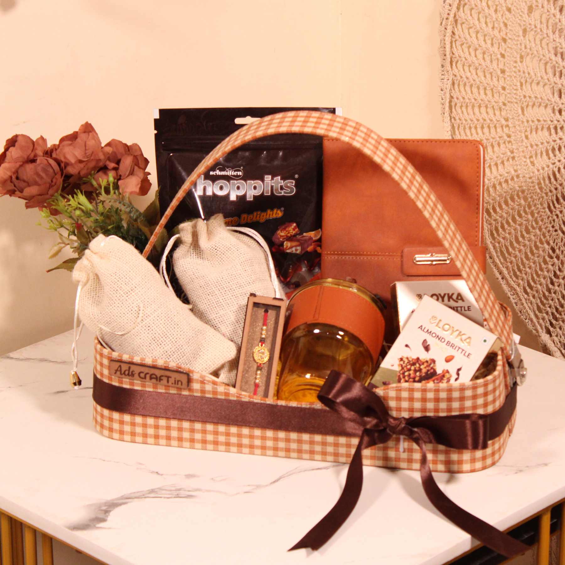 Rakhi gift hamper for brother in a brown check basket with dry fruits, Hoppits chocolate, and diary.